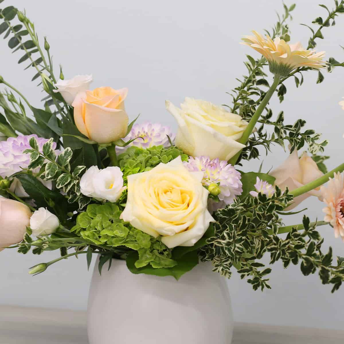 Peach and cream roses, green hydrangea, lisianthus and seasonal flowers in the Posy Peach arrangement
