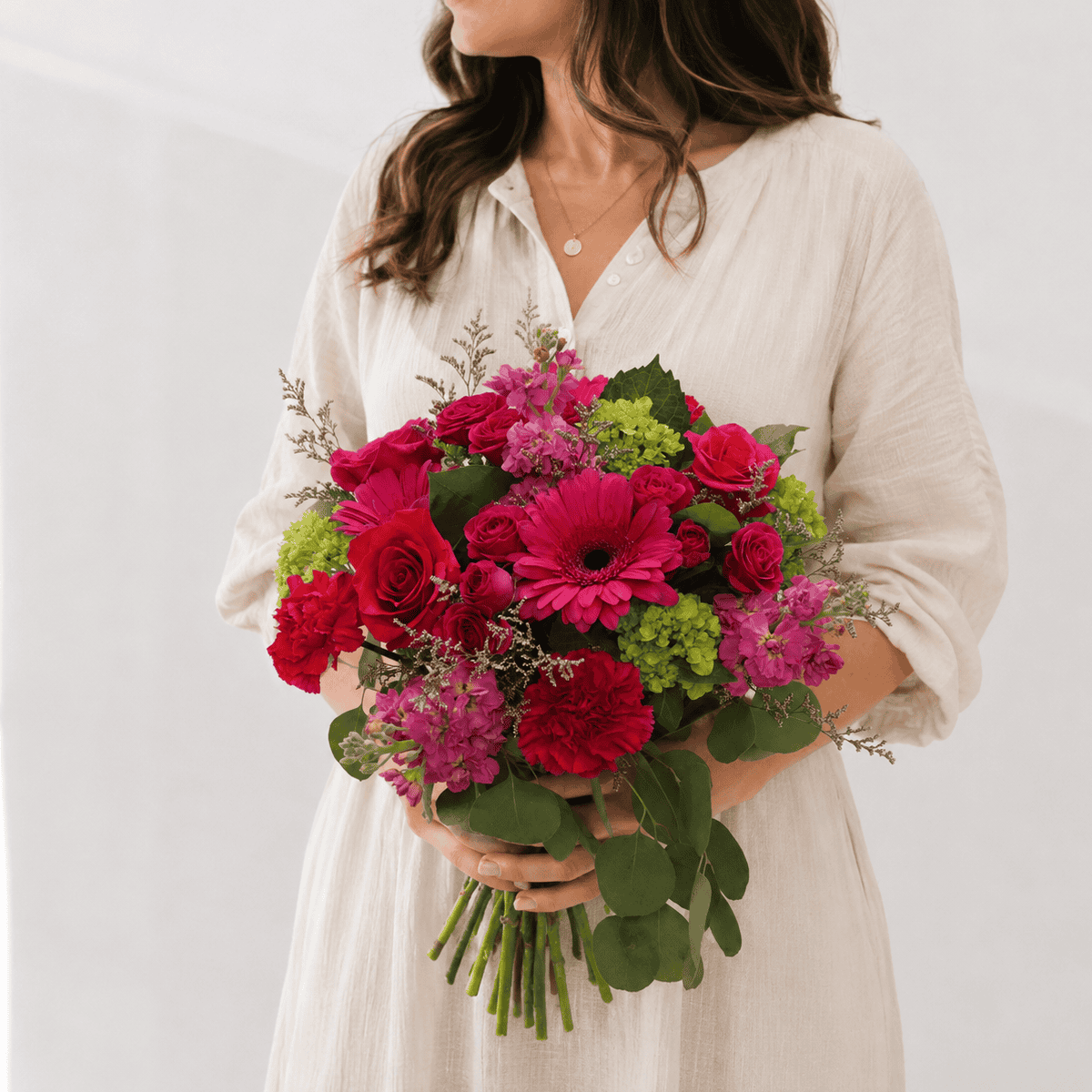 Woman holding the Raspberry Bloom bouquet with pink roses, gerbera daisies, carnations, hydrangea and eucalyptus.