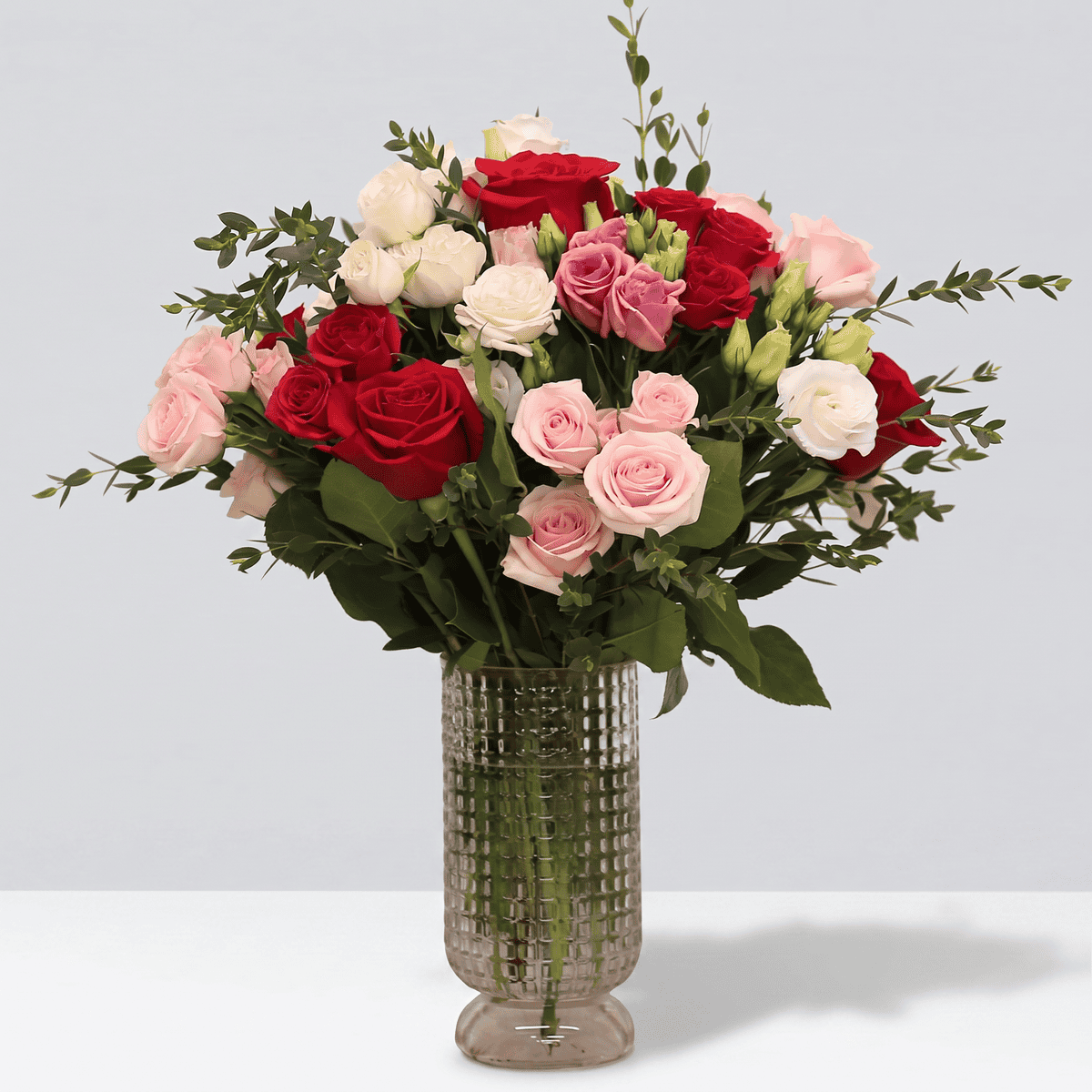 Sophia flower arrangement with Freedom roses, spray roses, lisianthus and eucalyptus in a pink textured glass vase.