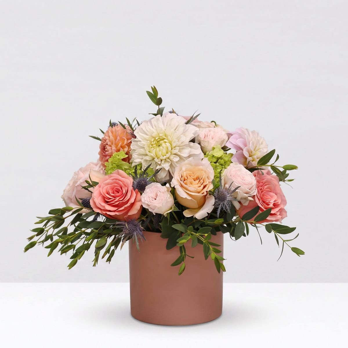 Summer Glow pink and peach floral arrangement with roses, seasonal dahlias, green hydrangea and blue eryngium in a rose vase