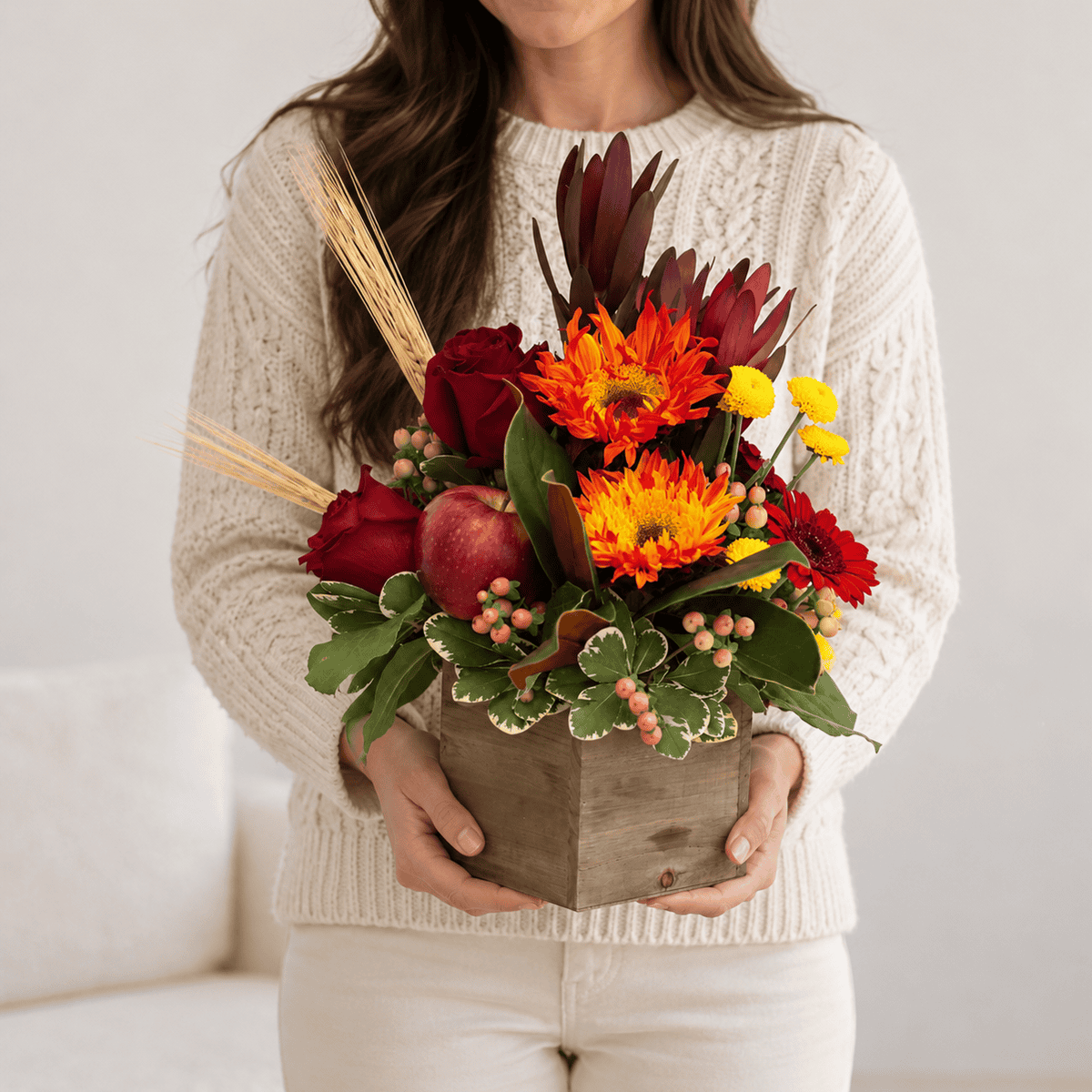 Autumn Orchard fall flower arrangement with red roses, apples and seasonal flowers held by a woman