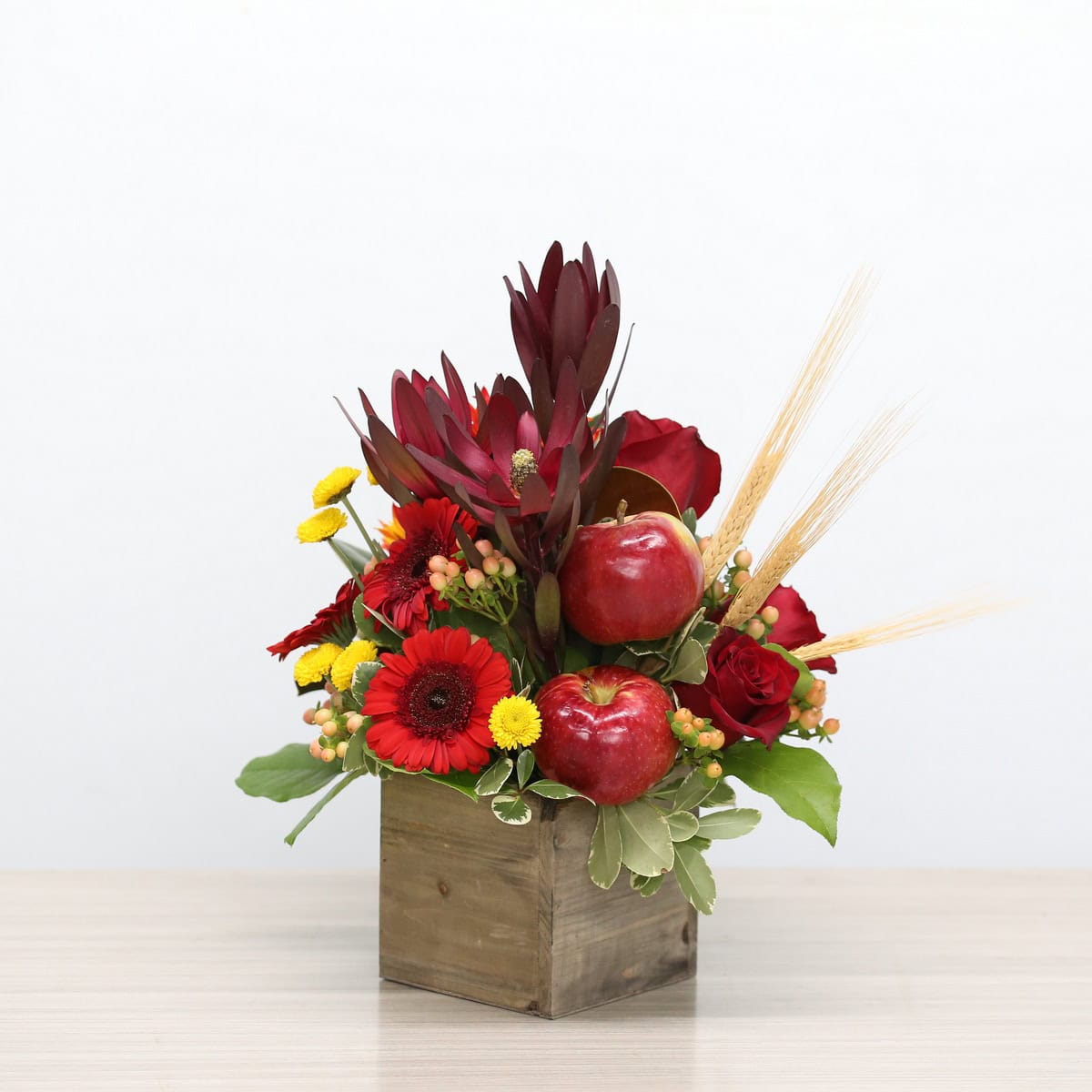 Autumn Orchard fall flower arrangement with red roses, gerberas, apples, wheat and seasonal foliage in a wooden box