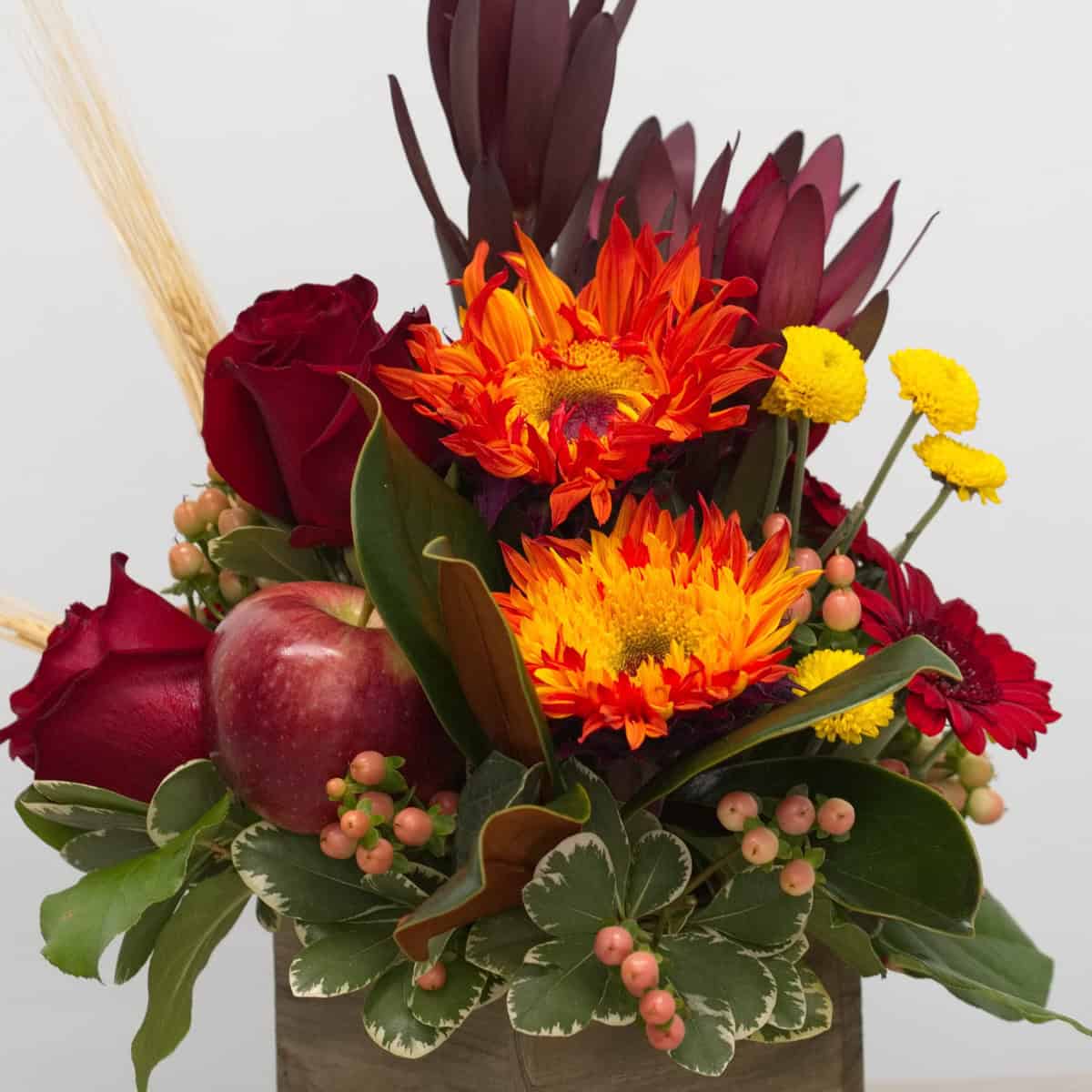 Close-up of Autumn Orchard with red roses, orange flowers, apples, berries and autumn greenery