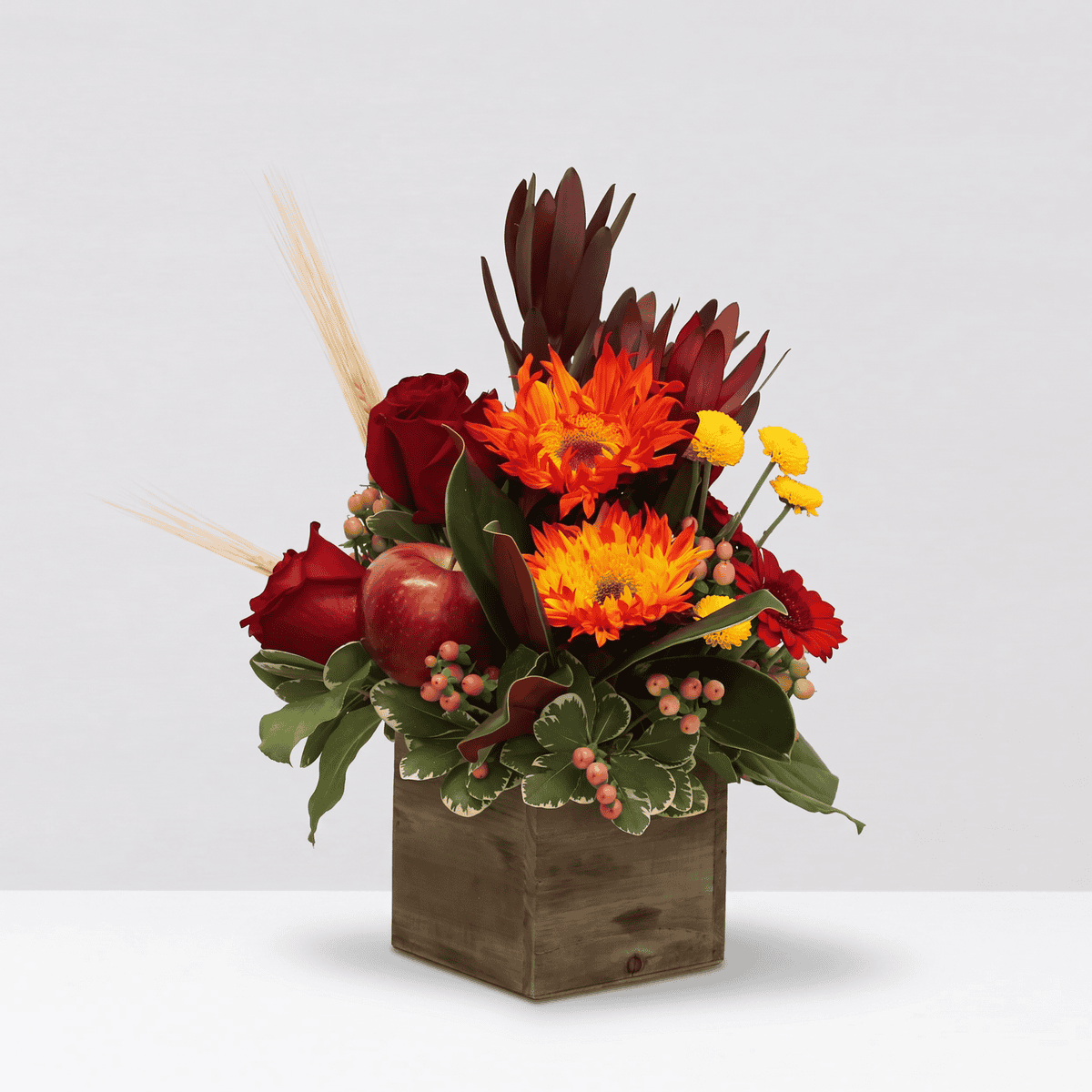 Autumn Orchard Thanksgiving flower arrangement with red roses, apples, orange flowers and wheat in a wooden box
