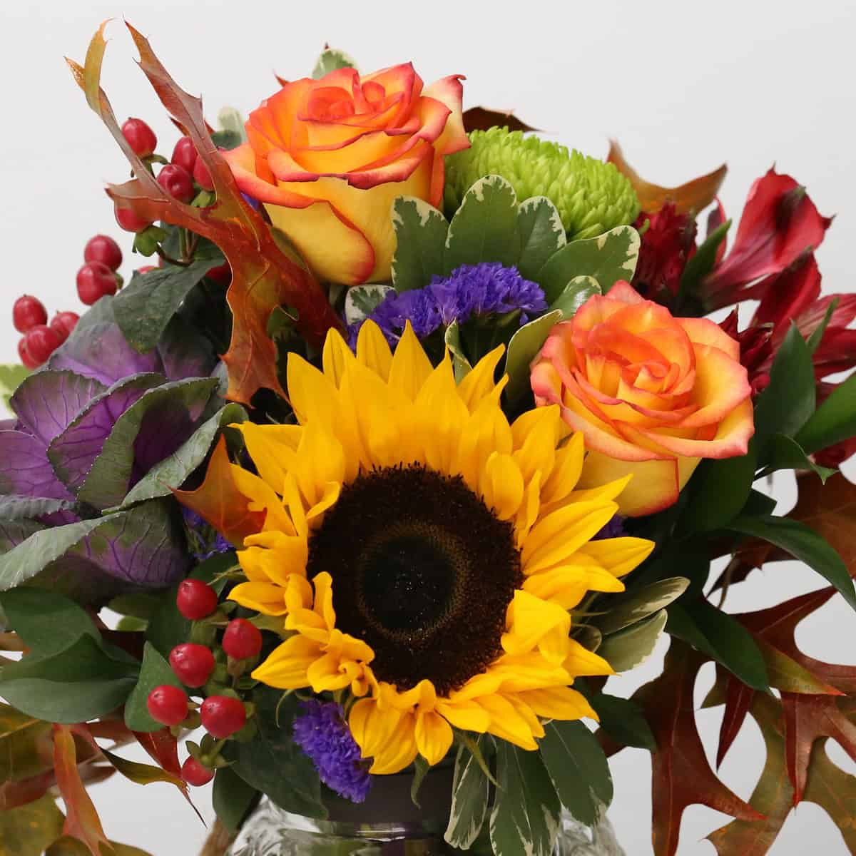 Close-up of Autumn fall flower arrangement with yellow sunflower, orange roses, purple ornamental kale and red berries