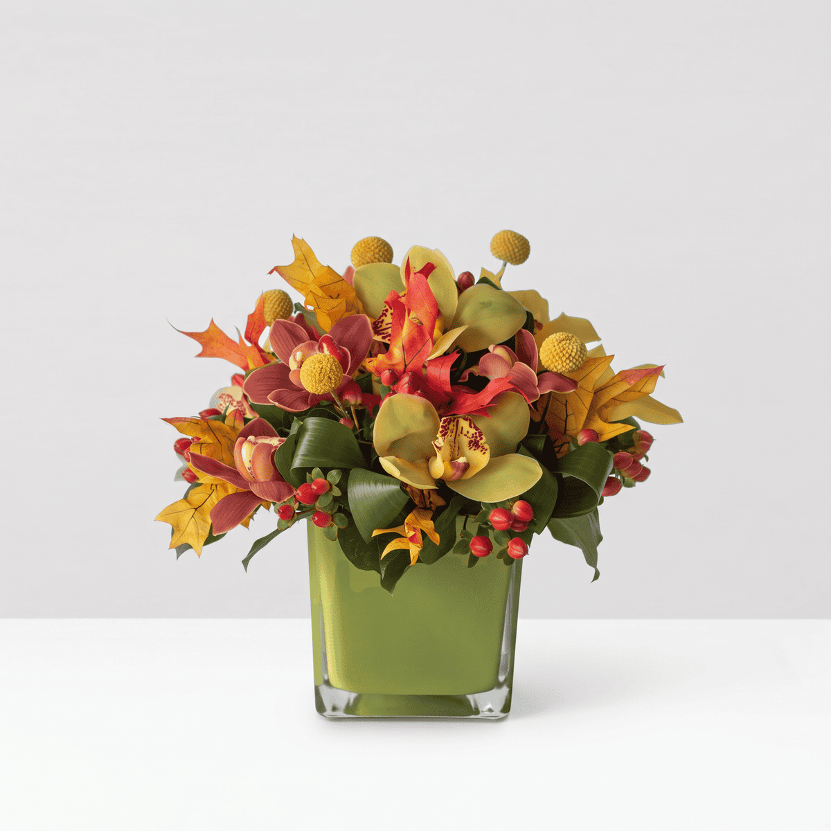Fall Orchid Symphony Deluxe arrangement with green and burgundy Cymbidium orchids, yellow craspedia and red berries in a green glass vase
