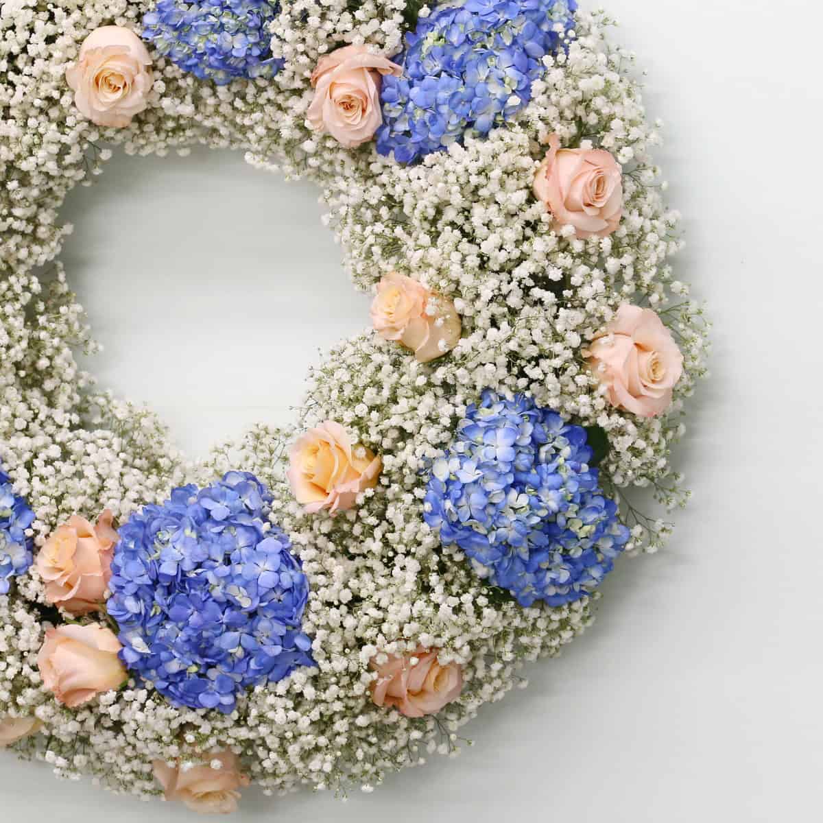 Close-up of Heavenly Clouds funeral wreath showing blue hydrangeas, pale pink roses and delicate white baby's breath.